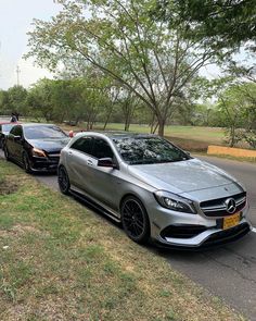 two mercedes cla parked on the side of the road next to each other in front of some trees