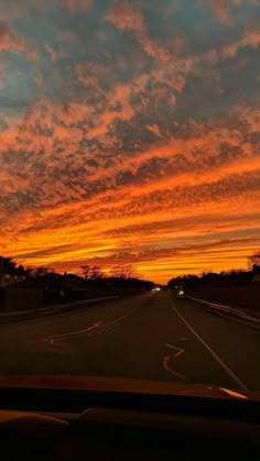 the sun is setting on an empty road with clouds in the sky and cars driving down it