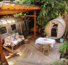 a patio with a couch, table and airstream in the back ground next to trees