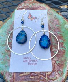 Silver hoop earrings with blue jasper stones. I am over the moon about these beauties! They are large and eye-catching but not too heavy! The stones are royal blue jasper. These earrings are 2 1/2 inches long and 1 1/2 inches wide. The French earwires are sterling silver. All my jewelry comes gift boxed with a custom Shelly Mariposa Design butterfly card ready for gift giving, whether it is a gift for you or someone special. Your satisfaction is very important to me. I make every effort to incor Nickel-free Blue Small Hoop Jewelry, Handmade Blue Hoop Jewelry, Hoop Earrings With Natural Stones For Gift, Blue Small Hoop Earrings With Matching Set, Blue Wire Wrapped Hoop Earrings, Blue Wire Wrapped Round Hoop Earrings, Blue Small Hoop Earrings Wire Wrapped, Blue Small Hoop Earrings With Wire Wrapping, Blue Teardrop Gemstone Hoop Earrings