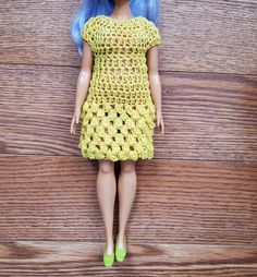 a doll with blue hair wearing a yellow crochet dress and green shoes on a wooden surface