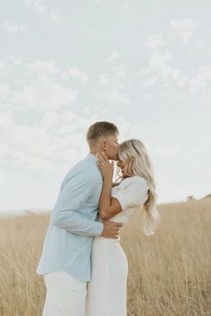 a man and woman kissing in the middle of an open field with tall grass behind them