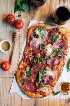 a pizza sitting on top of a wooden table next to some sauces and tomatoes