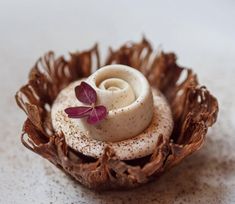 a white plate topped with a pastry covered in icing next to a purple flower