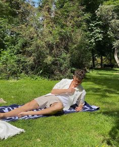 a man laying on top of a blue and white blanket in the grass next to trees