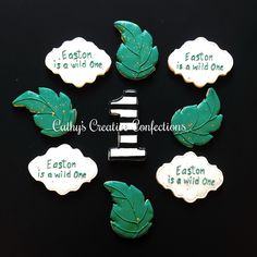 six cookies decorated with green leaves and white writing on black background that says each is a wild one