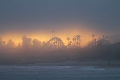 the sun is setting over an amusement park on a foggy day at the beach