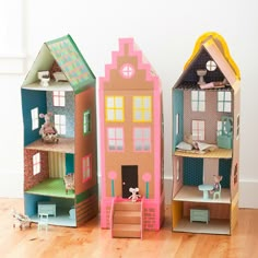 three wooden doll houses with windows and doors on the front, one has a cat in it