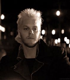 a black and white photo of a man with blonde hair wearing a leather jacket in the dark