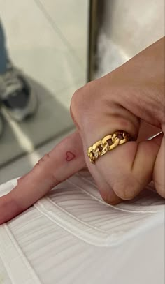 a person with a gold chain ring on their finger