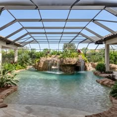 an outdoor pool with waterfall and rocks in the center, surrounded by glass roofing