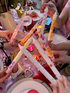 several people holding candles at a table with plates and napkins on it, all decorated in pink