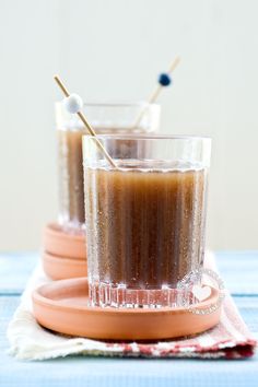 two glasses filled with liquid and toothpicks on top of each other, sitting on plates