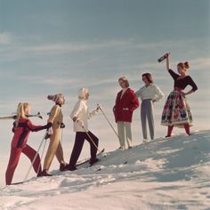 four women standing on top of a snow covered slope with skis and poles in their hands