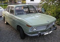 an old green car is parked on the gravel