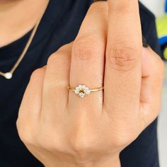 a woman wearing a gold ring with white flowers on it's middle finger, holding her right hand up to the camera