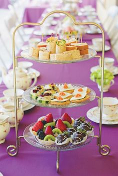 three tiered trays filled with food on top of a purple table cloth