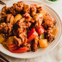 a white plate topped with meat and veggies next to chopsticks on a table