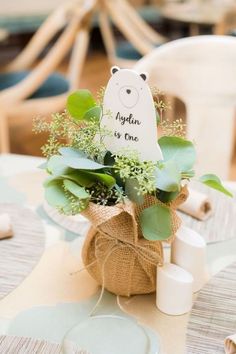 a table topped with a vase filled with greenery and a bear sign on top of it