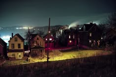 some houses are lit up at night in the city with lights shining on them and foggy hills behind them