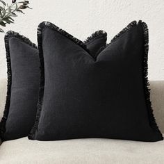 two black pillows sitting on top of a white couch next to a potted plant