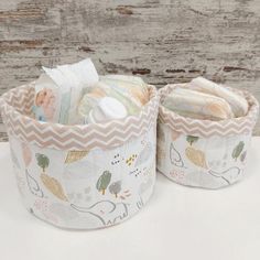 two baskets filled with baby items sitting on top of a white table next to a wooden wall