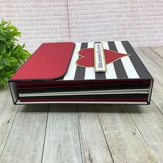 a red and black striped notebook sitting on top of a wooden table next to a potted plant