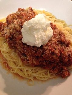 a white plate topped with spaghetti and meat covered in sour cream on top of it