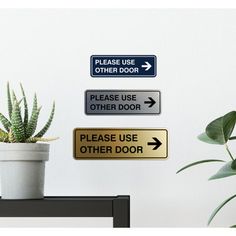 a potted plant sitting next to a sign that says please use other door and an arrow pointing in opposite directions