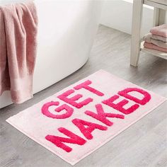 a bathroom rug that says get naked on the floor next to a bathtub with pink towels