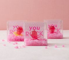 three clear boxes with pink candies in them on a white tablecloth covered surface