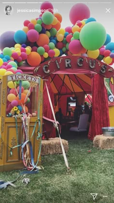 a bunch of balloons that are on the ground in front of a circus tent with hay bales