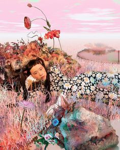 a woman laying on top of a pile of rocks in a field filled with flowers