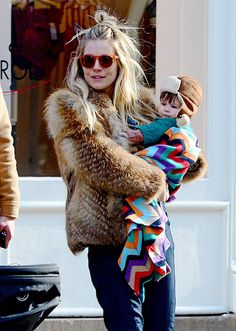 a woman holding a baby in her arms while walking down the street with other people