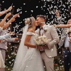 a bride and groom kiss as confetti falls around them