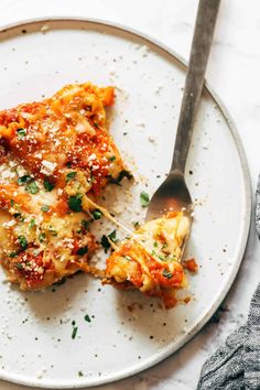 two pieces of lasagna on a white plate with a silver spoon and fork