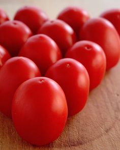 a bunch of red tomatoes sitting on top of a wooden cutting board next to each other