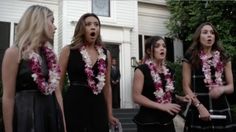 three women in black dresses standing outside with leis around their necks and one woman covering her mouth