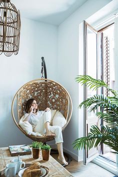 a woman sitting in a hanging chair with her feet up on the table next to a potted plant