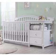 a baby crib with two drawers and a teddy bear sitting on the floor next to it