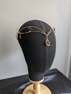 Beautiful gold wire circlet with red crystal bead accents. Perfect for renaissance fairs, weddings, cosplay, or any event of your choosing! This circlet features a delicate, yet sturdy design. Adjustable, one size fits most (adults and older children, not for toddlers or infants). Secured with a tied ribbon in the back.  For alternate colors of wire, beading, or ribbon, please message me for custom orders! Ribbon can also be substituted with adjustable size gold chain for back closure. Wire Circlet, Gold Circlet, Elven Headpiece, Circlet Crown, Elf Tiara, Elven Circlet, Crown Fairy, Wire Beading, Medieval Crown