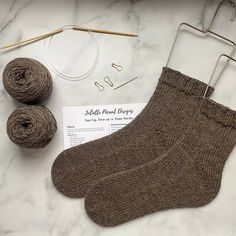 a pair of brown socks sitting on top of a table next to yarn and knitting needles