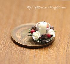 a small white candle sitting on top of a wooden table with pine cones and flowers