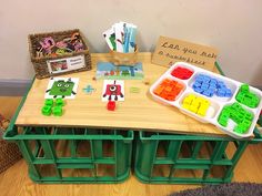 a wooden table topped with lots of legos on top of green trays next to a basket filled with pencils