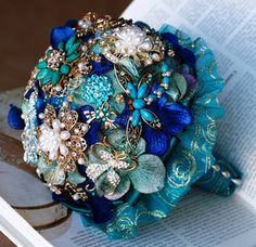 the brooch bouquet is sitting on top of an open book, with blue flowers and pearls