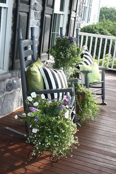 two rocking chairs sitting on top of a wooden deck next to plants and flowers in front of them