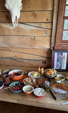 a wooden table topped with lots of bowls and plates filled with food next to a deer skull