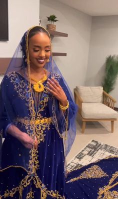 a woman in a blue and gold wedding dress smiles at the camera while standing next to a couch