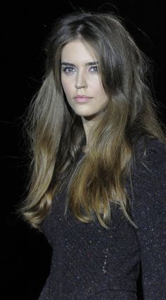 a woman with long brown hair and blue eyes is looking at the camera while standing in front of a black background