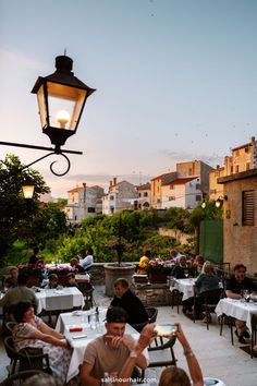 people are sitting at tables outside in the evening